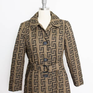 May include: A long brown quilted coat with a black geometric pattern and a black belt. The coat has a collar and four black buttons.