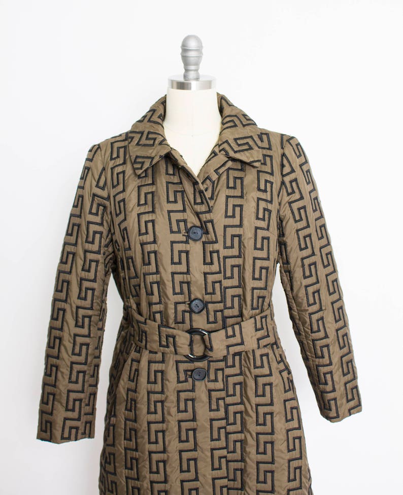 May include: A long brown quilted coat with a black geometric pattern and a black belt. The coat has a collar and four black buttons.