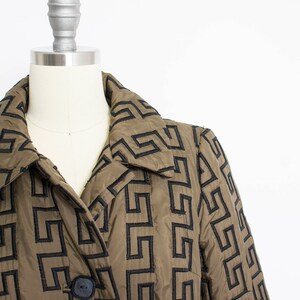 May include: A brown quilted jacket with a black geometric pattern. The jacket has a collar and a button closure.