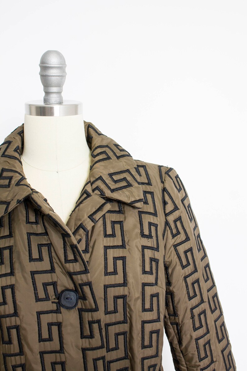 May include: A brown quilted jacket with a black geometric pattern. The jacket has a collar and a button closure.