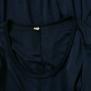 Puede incluir: Una camisa azul marino de manga larga con cuello redondo. La camisa tiene una peque&ntilde;a etiqueta blanca con el texto "M" y "Hecho en China" en ella.