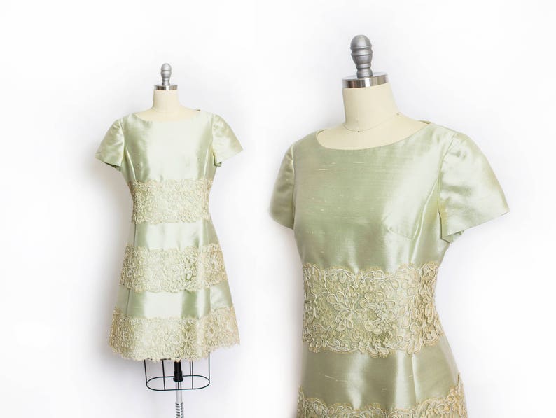 May include: A light green dress with a lace trim and a layered skirt. The dress has short sleeves and a fitted bodice.