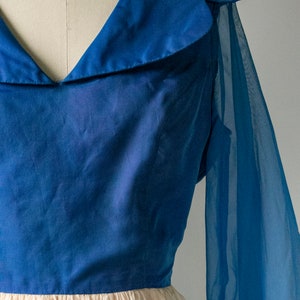 May include: A blue dress with a sheer overlay and a large collar. The dress has a fitted bodice and a full skirt.