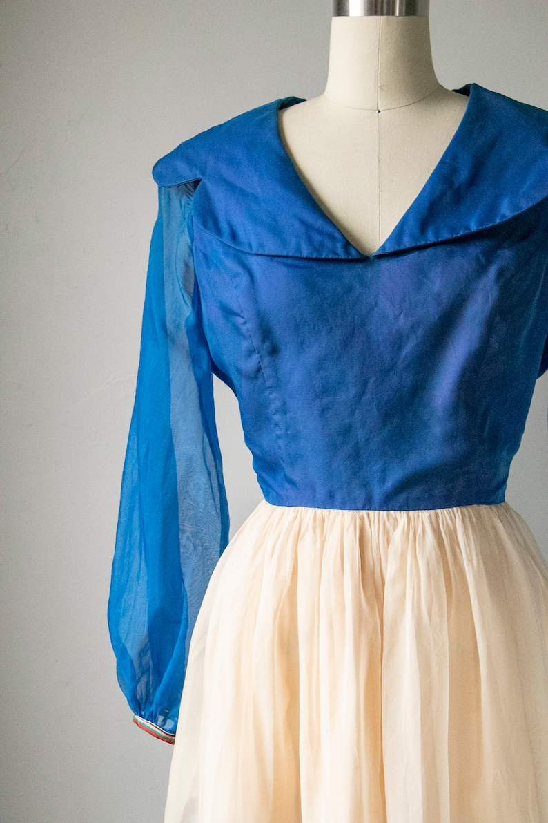 May include: A vintage dress with a blue bodice and a white tulle skirt. The bodice has a wide, sailor-style collar and long sleeves.