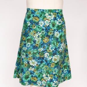 May include: A-line skirt with a vibrant floral pattern in shades of green, blue, and white. The skirt is displayed on a mannequin, showcasing its shape and design. The fabric appears to be a lightweight material.
