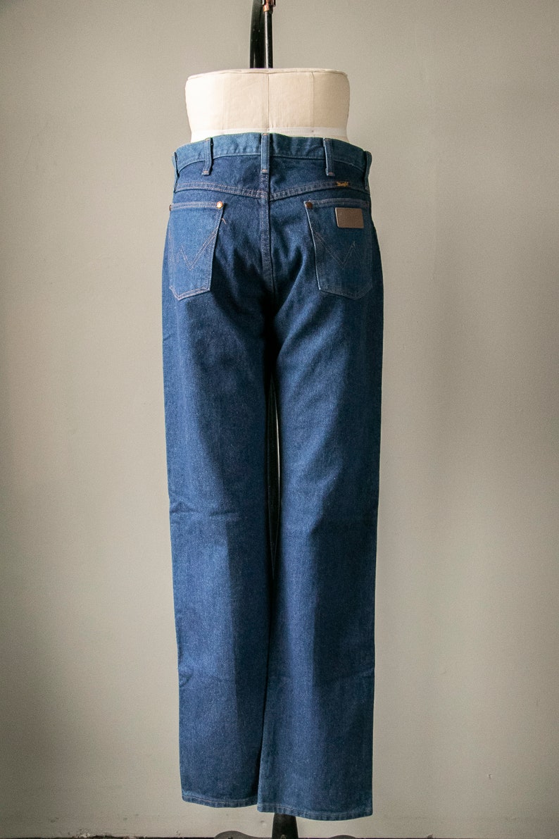 Puede incluir: Un par de pantalones vaqueros azules de mezclilla con un parche de cuero marr&oacute;n en el bolsillo trasero. Los pantalones est&aacute;n en un maniqu&iacute;.
