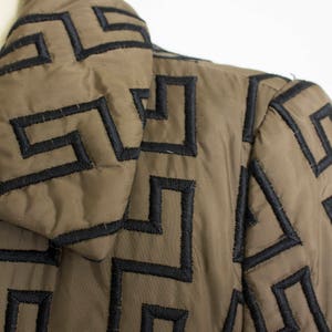 May include: A brown quilted jacket with a black geometric pattern. The jacket has a high collar and a zip closure.