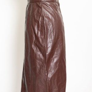 May include: A brown leather skirt with a high waist and a knee-length hem. The skirt is made of a smooth, shiny leather material and has a classic, tailored design. The skirt is displayed on a mannequin.