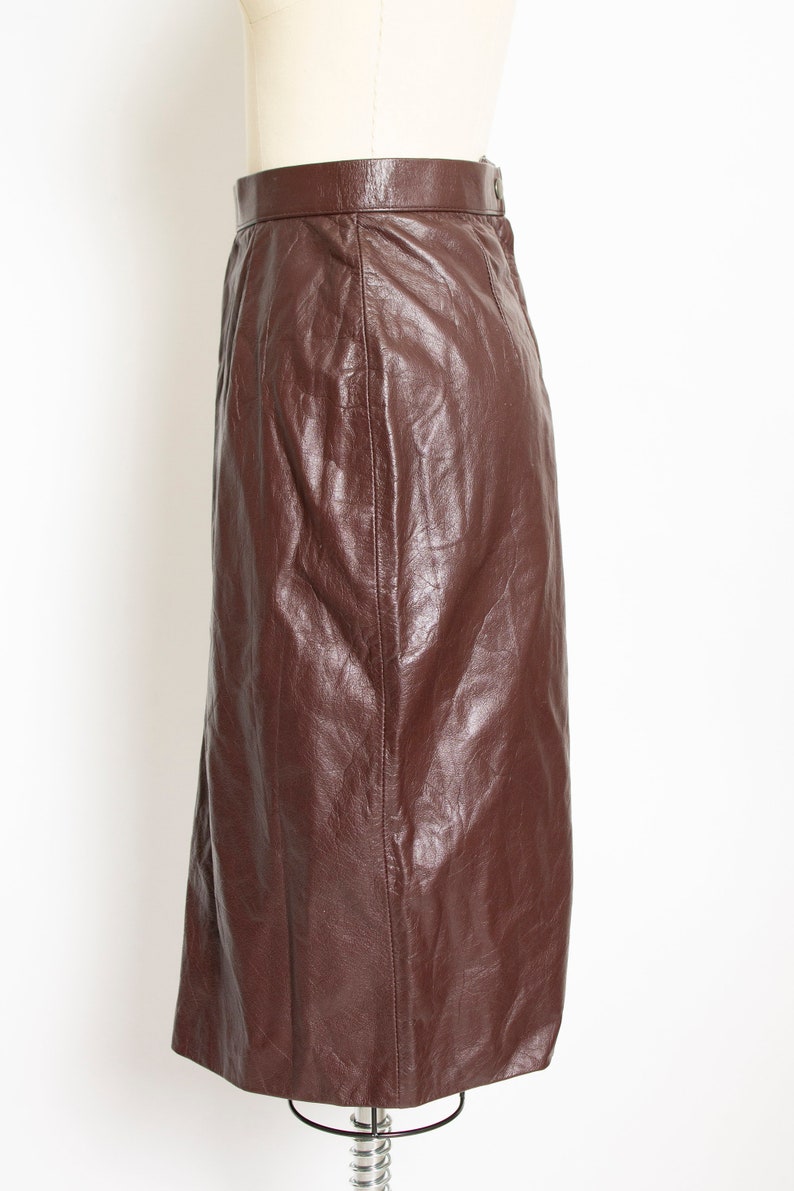 May include: A brown leather skirt with a high waist and a knee-length hem. The skirt is made of a smooth, shiny leather material and has a classic, tailored design. The skirt is displayed on a mannequin.