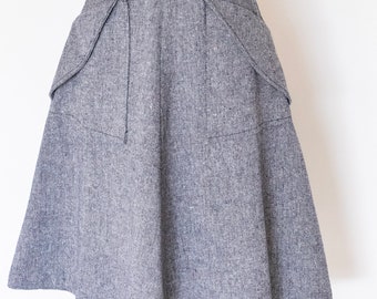 May include: A gray, knee-length skirt with two large pockets on the front. The skirt is made of a textured fabric and has a fitted waistband.