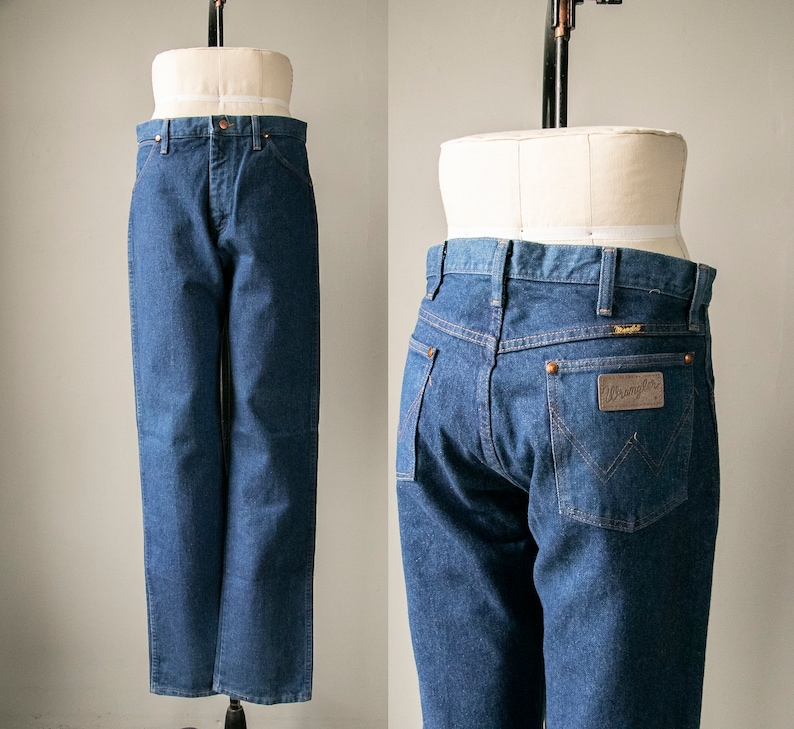 Puede incluir: Un par de pantalones vaqueros azules de mezclilla con un corte cl&aacute;sico de pierna recta. Los pantalones tienen un parche de cuero marr&oacute;n con el logotipo de Wrangler en el bolsillo trasero derecho.