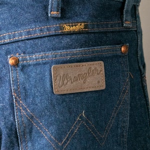 Puede incluir: Un par de pantalones vaqueros azules con un parche de cuero marr&oacute;n en el bolsillo trasero que dice "Wrangler".