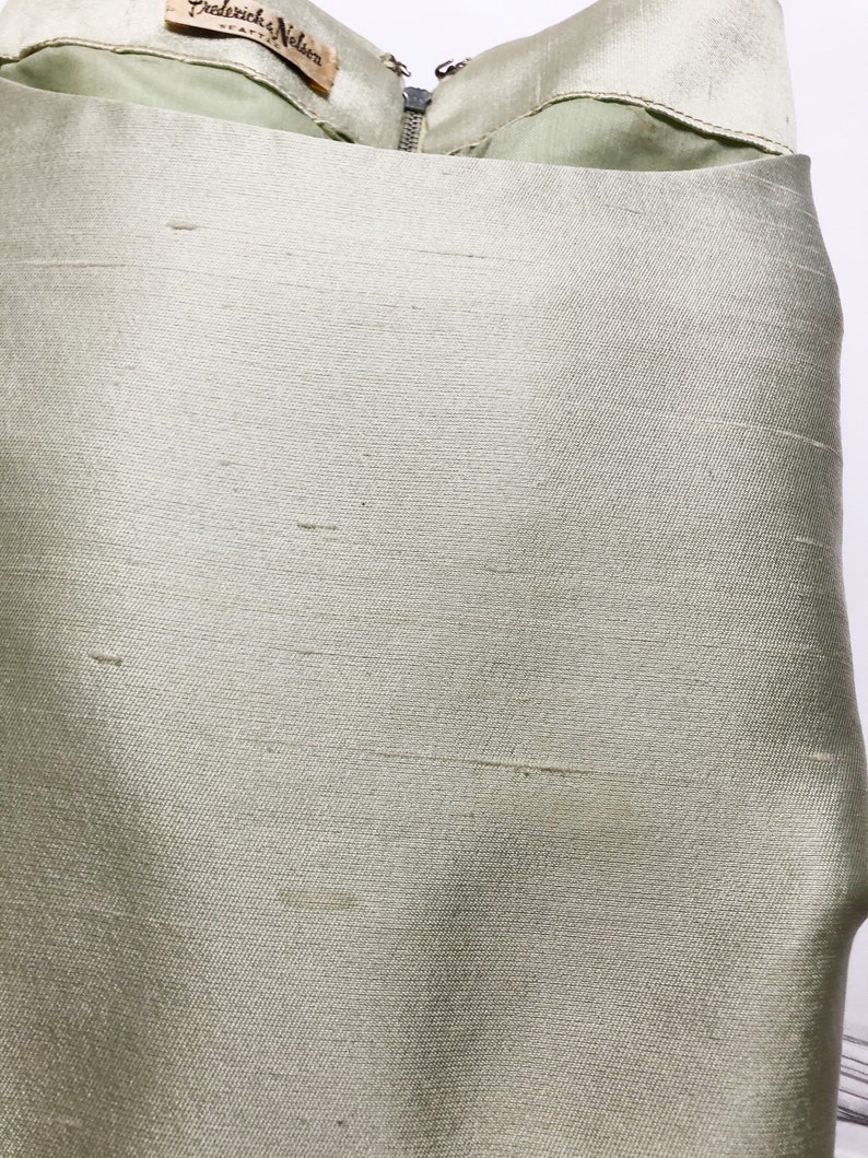 May include: A light green satin skirt with a zipper closure and a label that reads "Frederick Nelson" in black text.