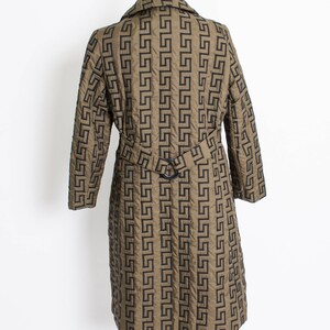 May include: A long, brown quilted coat with a black geometric pattern. The coat has a belt and long sleeves.