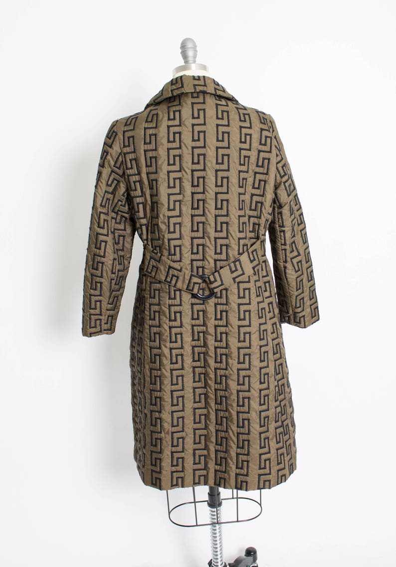 May include: A long, brown quilted coat with a black geometric pattern. The coat has a belt and long sleeves.