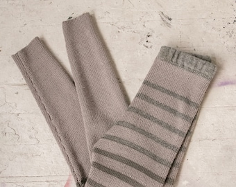 May include: A pair of gray striped knit leggings with a ribbed texture. The leggings are folded in half and laid flat on a white surface.