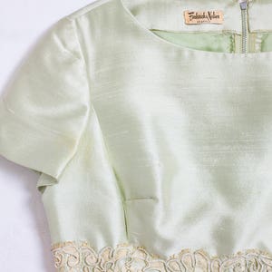 May include: A light green dress with a lace trim and a label that reads "Frederick & Nelson Seattle".