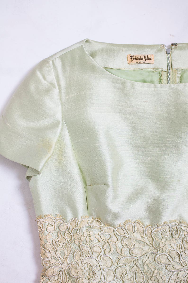 May include: A light green dress with a lace trim and a label that reads "Frederick & Nelson Seattle".