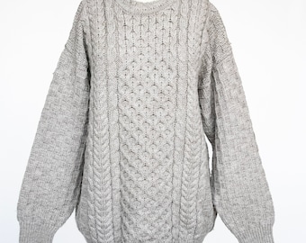 May include: A gray cable knit sweater with a crew neck. The sweater is made of a soft, warm material and has a relaxed fit.