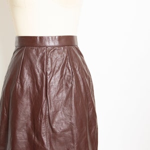 May include: A dark brown leather skirt displayed on a mannequin. The skirt has a high waist and a knee-length hemline. The leather has a slightly wrinkled texture, and the skirt appears to be well-made.