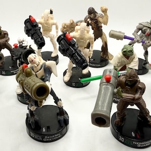 May include: A collection of ten Star Wars plastic action figures standing on black circular bases. The figures include characters like General Grievous, Yoda, and various soldiers, each holding weapons such as blasters, cannons, or lightsabers.