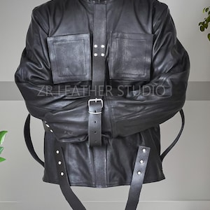 Könnte beinhalten: Schwarze Lederjacke mit hohem Kragen, zwei Vordertaschen und einem zentralen Riemen mit Schnalle. Die Jacke hat Riemen, die sich von den Ärmeln und dem Saum erstrecken. Der Text "ZR LEATHER STUDIO" ist auf der Jacke zu sehen.