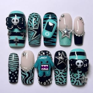 May include: A set of ten artificial nails with various designs. The nails feature a mix of teal, black, and white colors. Some nails have skull and bow accents, while others have star, zebra, and leopard print patterns. One nail has a small teal MP3 player.