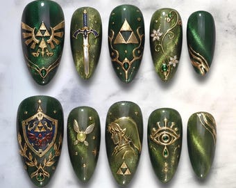 Unghie finte ispirate a Zelda, unghie fantasy verde scuro e oro, nail art Triforza, unghie da gamer di Zelda, unghie fantasy 3D