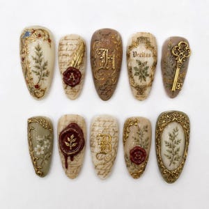Pode incluir: Um conjunto de dez unhas postiças em formato de amêndoa com designs intrincados de inspiração vintage. As unhas apresentam fundos creme, bege e verde sálvia com filigrana dourada, selos de cera, escrita cursiva e uma chave dourada.