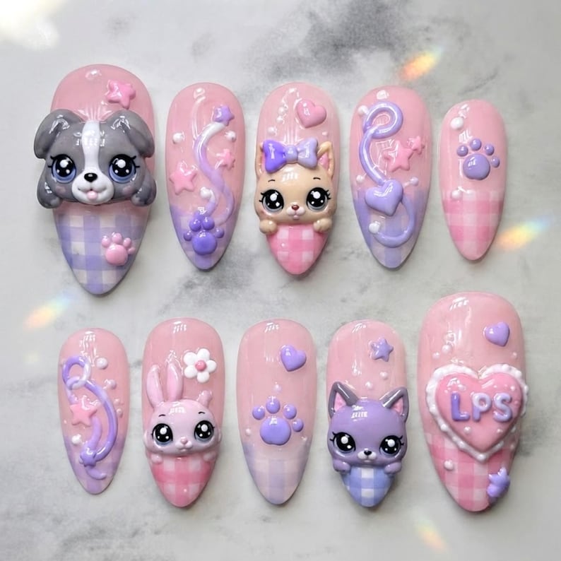 May include: A set of ten press-on nails featuring a pink and purple gingham pattern. The nails are decorated with 3D charms including animal faces, paw prints, stars, hearts, and flowers. One nail features a heart-shaped charm with the letters LPS.