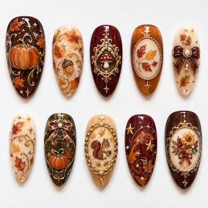 May include: A set of ten almond-shaped press-on nails featuring intricate 3D autumn-themed designs. The collection includes motifs of pumpkins, acorns, mushrooms, squirrels, sunflowers, bows, and fall leaves, accented with gold filigree frames.