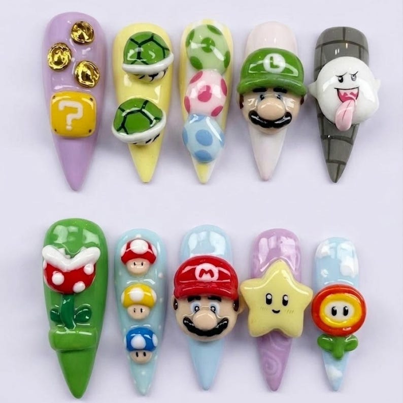 May include: A set of ten press-on nails featuring 3D sculpted designs inspired by video game characters and items, including Mario, Luigi, a ghost, mushrooms, stars, shells, and a question block, all rendered in vibrant colours on various base shades.