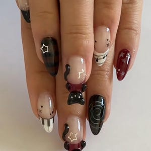 May include: A hand with a set of long, almond-shaped nails. The nails feature various designs, including a piano keyboard, musical notes, stars, and abstract black shapes. Some nails have a clear base with black tips.
