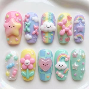 Könnte beinhalten: Zehn farbenfroh dekorierte Acrylnägel. Jeder Nagel zeigt ein anderes Design, darunter Sterne, Wolken, Regenbogen und Blumen. Die Nägel sind in Pastellfarben mit 3D-Verzierungen bemalt, was eine skurrile und verspielte Ästhetik erzeugt.