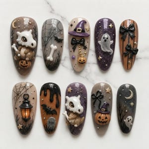 May include: A set of ten press-on nails featuring Halloween and creature-themed 3D designs. The nails display motifs including a skull-headed creature, pumpkins, ghosts, bats, spiderwebs, lanterns, tombstones, bows, stars, and crescent moons.