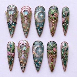Pu&ograve; includere: Un set di dieci unghie finte a mandorla con intricati disegni in 3D. I motivi includono figure di fate iridescenti, lune crescenti con stelle, alberi dettagliati con fiori rosa e un rigoglioso fogliame verde con piccoli funghi.