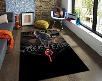 May include: A rectangular black area rug with a detailed graphic design. The rug features a central image of a pendant with a red eye, and a dark, detailed background. The rug is placed on a wooden floor in a living room setting.