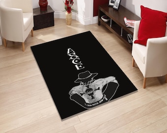 May include: Black rectangular rug with a white illustration of a character wearing a hat and the word "ACE". The rug is on a light wood floor. The rug is suitable for a living room.