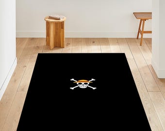 May include: Black rectangular rug with a white skull and crossbones design, topped with a straw hat. The rug is placed on a light wood floor. A small wooden table and stool are visible in the background.