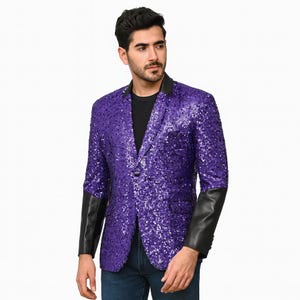 Può includere: Un blazer di paillettes viola con maniche in pelle nera e colletto nero. Il blazer ha una chiusura con un solo bottone e due tasche anteriori. Il capo è indossato sopra una camicia nera.