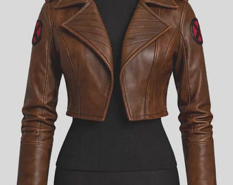 May include: A cropped brown jacket with long sleeves and a wide collar. The jacket features a circular black and red X-Men logo patch on each shoulder. The design includes structured paneling on the front and sleeves, with a smooth finish.
