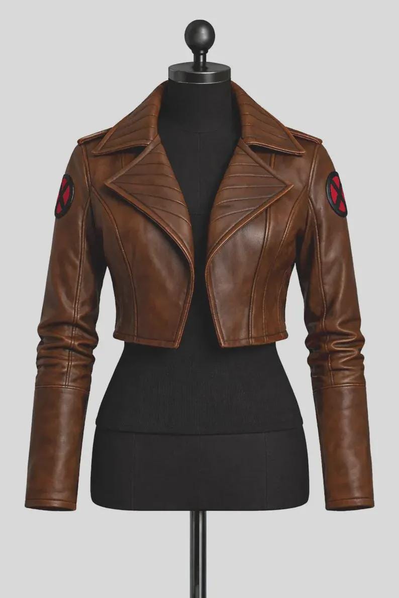 May include: A cropped brown jacket with long sleeves and a wide collar. The jacket features a circular black and red X-Men logo patch on each shoulder. The design includes structured paneling on the front and sleeves, with a smooth finish.