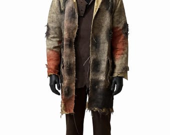 May include: A distressed, knee-length coat made of coarse, tan-coloured fabric with frayed edges, dark brown and rust-coloured patches, and visible wear. The coat is worn over a dark brown shirt and dark brown trousers, paired with black shoes.