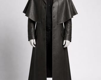 May include: A dark grey leather coat with a cape-like shoulder design. The long coat features a button-down front, a notched collar, and a tailored fit. The mannequin is wearing a black shirt, trousers, and shoes.