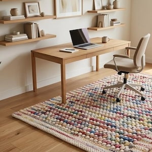 May include: A rectangular area rug featuring a textured, multi-coloured pom-pom surface with a woven border. The rug displays a vibrant mix of pastel and primary colours, including blue, red, yellow, and green, arranged in a repeating pattern.