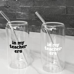Könnte beinhalten: Zwei transparente Glasbecher mit gebogenen Glasstrohhalmen. Jeder Becher trägt den schwarzen Aufdruck "in my teacher era". Die Becher sind zylindrisch und stehen auf einer weißen Oberfläche.