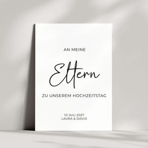 Può includere: Un cartello rettangolare bianco con testo nero che recita AN MEINE Eltern ZU UNSEREM HOCHZEITSTAG 10 JULI 2027 LAURA & DAVID. La parola Eltern è scritta in un grande ed elegante carattere corsivo, mentre il resto è in un carattere sans-serif.