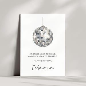 Könnte beinhalten: Eine weiße Geburtstagskarte mit einer silbernen Discokugel-Illustration im oberen Bereich. Der Text lautet: ANOTHER YEAR TO SHINE, ANOTHER YEAR TO SPARKLE. HAPPY BIRTHDAY, Marie. Das Design ist auf einem klaren, weißen Hintergrund zentriert.