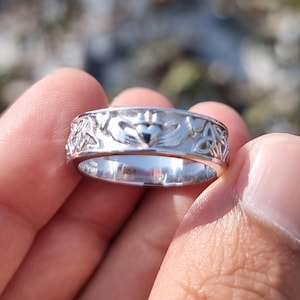 May include: A silver-toned metal ring featuring a Claddagh design with a central heart held by two hands and topped with a crown, flanked by intricate Celtic knotwork patterns around the entire band, with the text AnkitDiamondJewels visible.