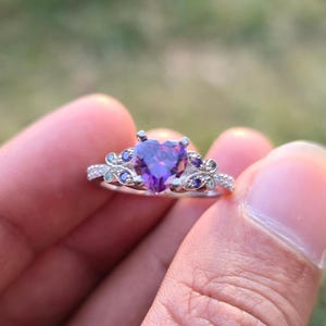 May include: A silver ring with a heart-shaped purple gemstone at the center, flanked by smaller blue and clear stones. The ring has a delicate, ornate design. The brand name "Ankit Diamond Jewels" is visible at the bottom of the image.